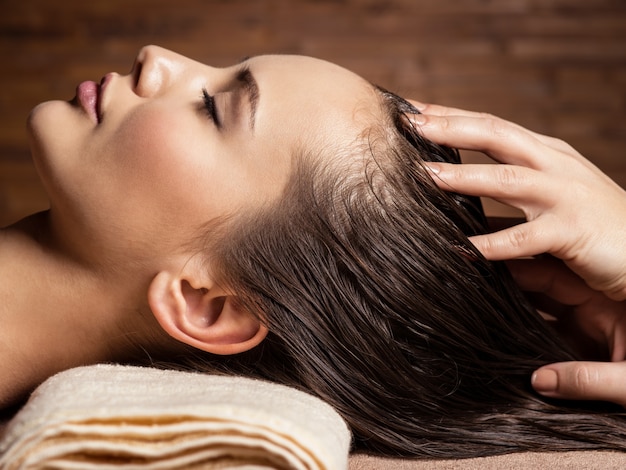 Masajista haciendo masaje en la cabeza y el cabello de una mujer en el salón de spa