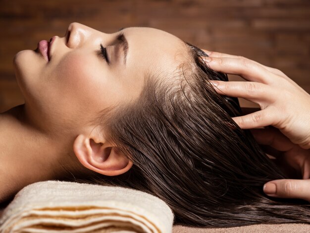 Masajista haciendo masaje en la cabeza y el cabello de una mujer en el salón de spa