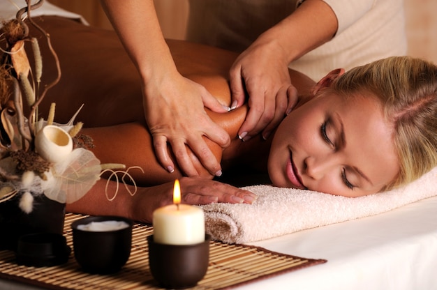 Masajista haciendo masaje en el hombro femenino en el salón de belleza