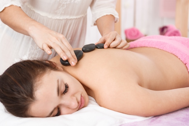 Masajista haciendo masaje con piedras calientes en espalda de mujer