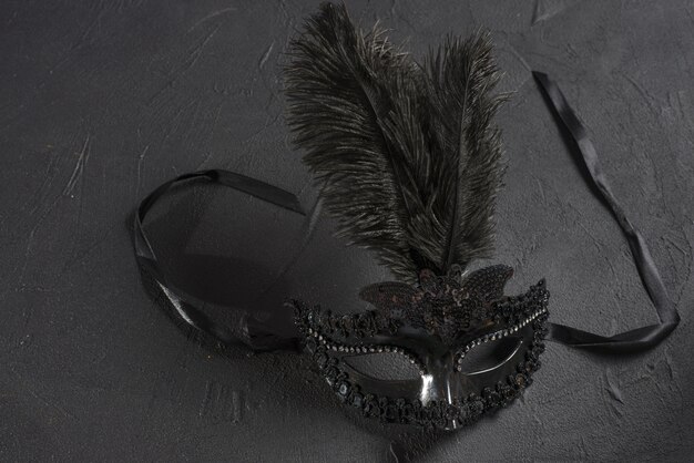 Máscara de carnaval con pluma en mesa negra.