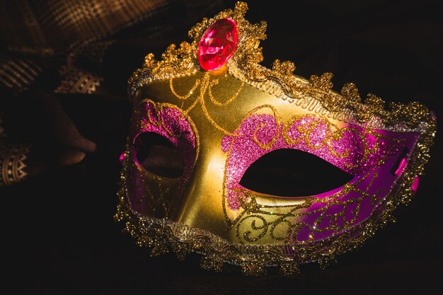 Máscara veneciana dorada y rosa sobre un fondo oscuro