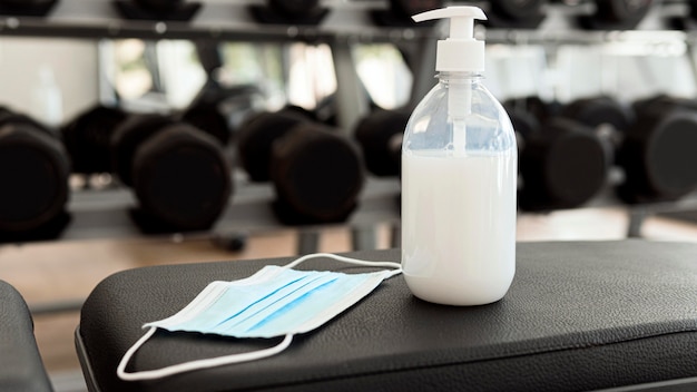 Foto gratuita mascarilla médica y desinfectante de manos en banco de gimnasio