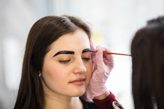 Master con pincel haciendo maquillaje con líneas de cejas anchas y negras