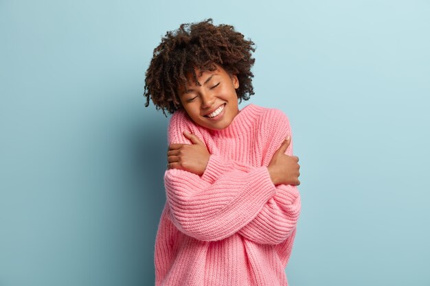 Ámate a ti mismo concepto. Foto de hermosa mujer sonriente se abraza a sí misma, tiene alta autoestima, cierra los ojos por placer