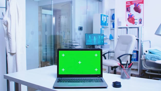 Material de archivo de computadora portátil con pantalla verde en el hospital Médico con abrigo llegando a la clínica de salud y enfermera trabajando en equipo en el gabinete. Cuaderno con pantalla reemplazable en clínica médica.