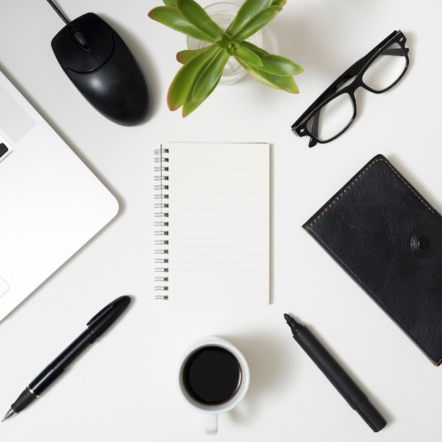 Material de oficina; ordenador portátil; taza de café y anteojos sobre fondo blanco