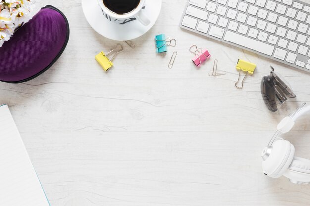 Material de oficina; taza de café; auriculares y teclado en el escritorio blanco