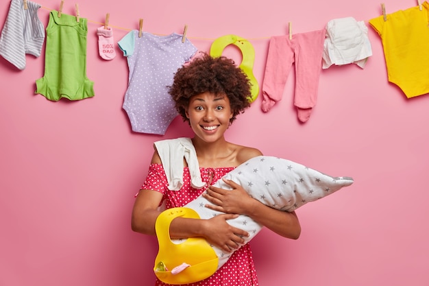 Maternidad, paternidad, concepto de cuidado infantil. Feliz joven madre lleva a bebé en brazos, sostiene babero, posa