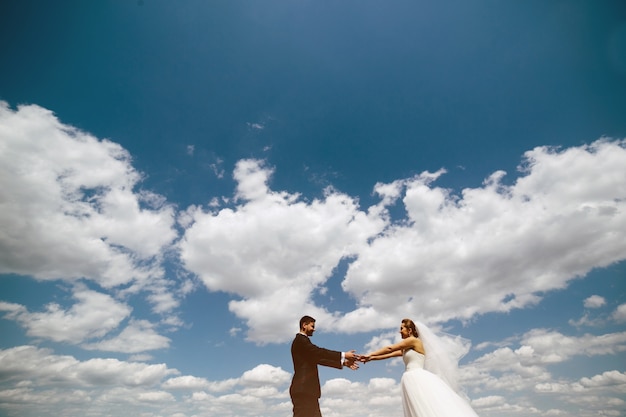 Matrimonio tomados de las manos con nubes en el cielo