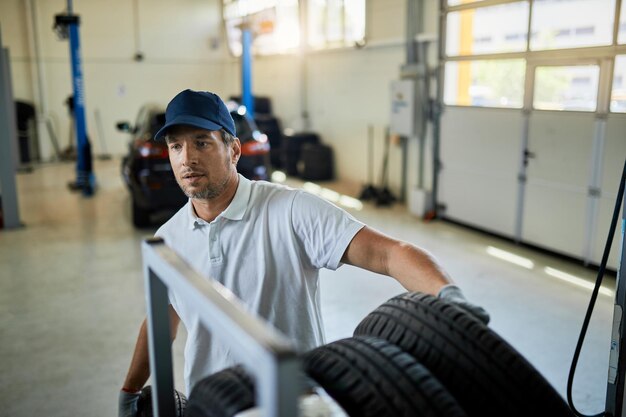 Mecánico adulto medio apilando neumáticos de automóviles mientras trabaja en un taller de reparación de automóviles