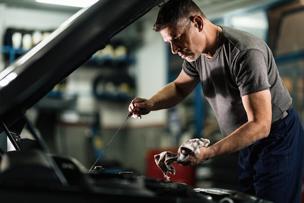 Mecánico adulto medio examinando aceite de coche en taller de reparación de automóviles