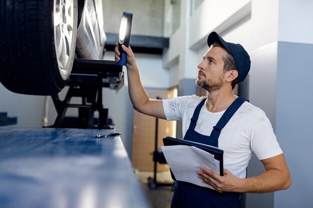 Mecánico adulto medio que usa una linterna mientras examina un automóvil en un taller de reparación de automóviles