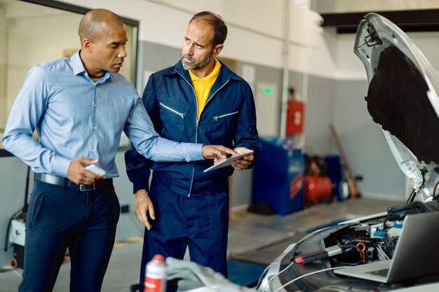 Mecánico adulto medio y su cliente usando el panel táctil en el taller de reparación de automóviles