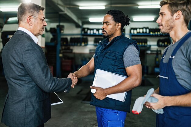 Mecánico de automóviles afroamericano estrechándole la mano a un gerente en un taller de reparación de automóviles