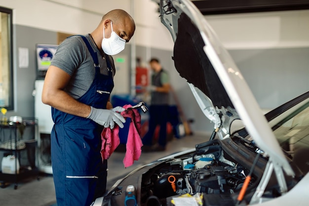 Foto gratuita mecánico de automóviles afroamericano con mascarilla protectora mientras trabaja en un taller