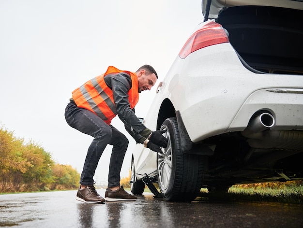 Mecánico de automóviles de emergencia cambiando neumático pinchado en la carretera