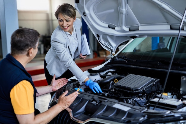 Foto gratuita mecánico de automóviles y empresaria cooperando mientras revisa bajo el capó del vehículo en un taller