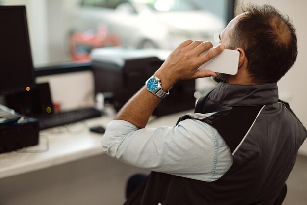 Mecánico de automóviles hablando por teléfono en la oficina del taller