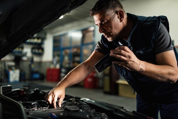 Mecánico de automóviles con lámpara mientras repara el motor en un taller