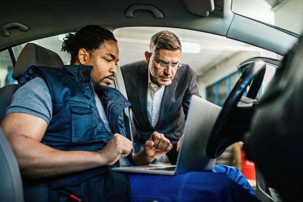 Mecánico de automóviles negro joven que usa la computadora con su gerente en el taller de reparación de automóviles