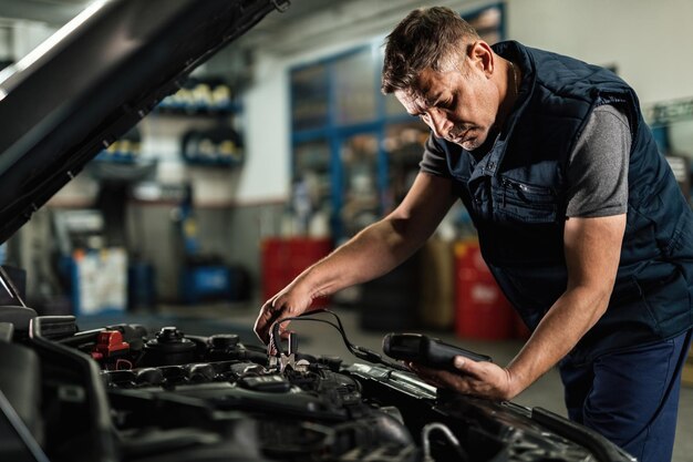 Mecánico de automóviles que usa una herramienta de diagnóstico mientras verifica el voltaje de la batería del automóvil en un taller