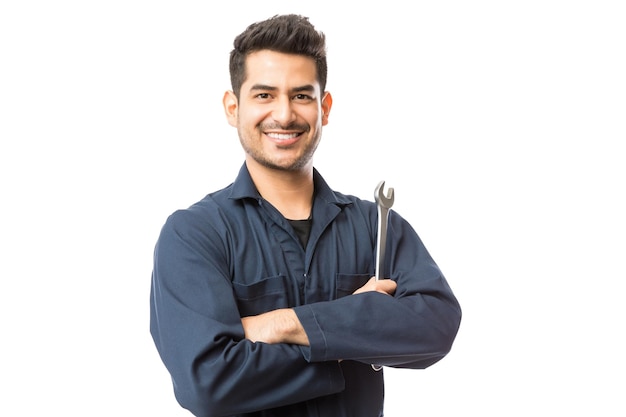 Mecánico de automóviles sonriente con llave de pie manos dobladas sobre fondo blanco.