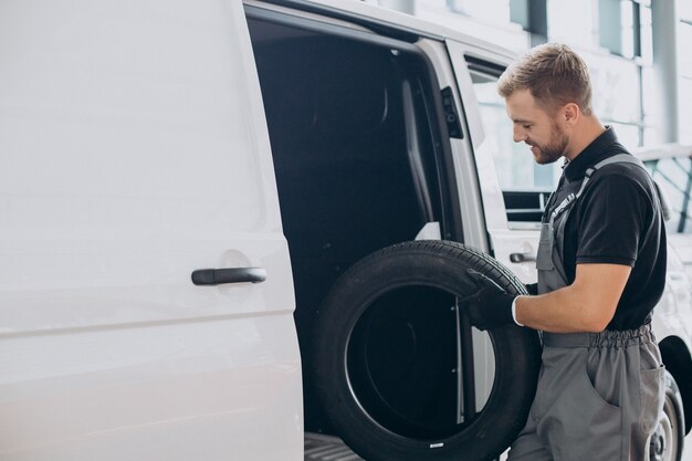 Mecánico de automóviles sosteniendo neumáticos nuevos por la camioneta blanca