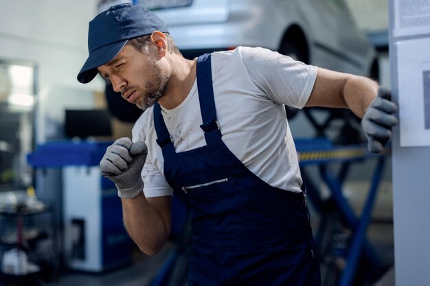 Mecánico de automóviles tosiendo mientras trabajaba en el taller de reparaciones