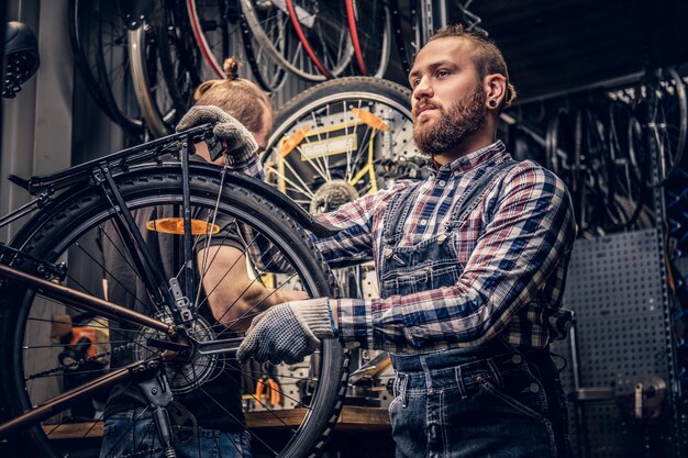 Mecánico barbudo de cabeza roja que fija el desviador trasero de una bicicleta en un taller.