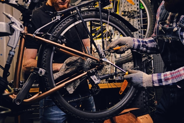 Mecánico barbudo de cabeza roja que fija el desviador trasero de una bicicleta en un taller.