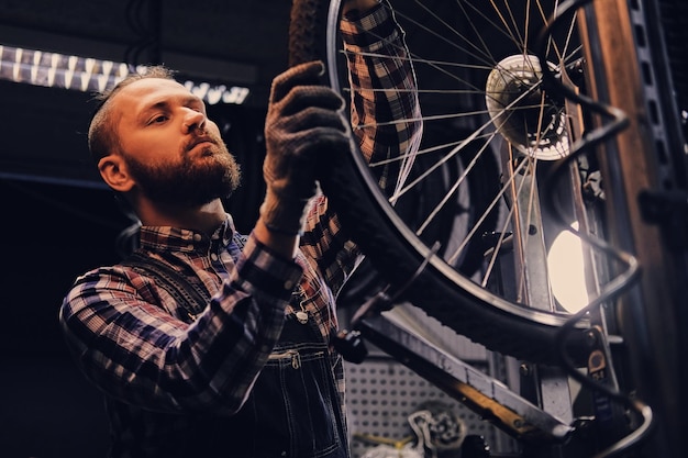Mecánico barbudo haciendo manual de servicio de rueda de bicicleta en un taller.