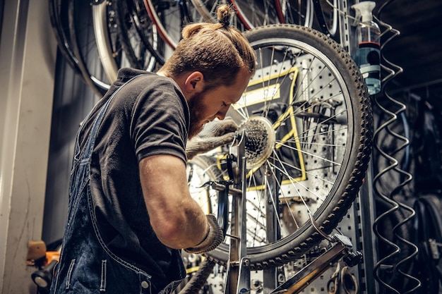 Mecánico barbudo de pelo rojo quitando el casete trasero de la bicicleta en un taller.