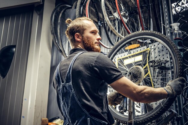 Mecánico barbudo reparando neumáticos de ruedas de bicicleta en un taller. Vista posterior, manual de servicio.