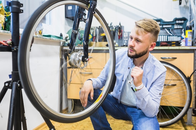 Mecánico de bicicletas con llave mirando neumáticos de bicicleta