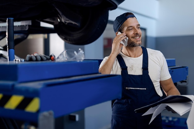 Mecánico feliz hablando por teléfono mientras trabaja en el taller de reparación de automóviles