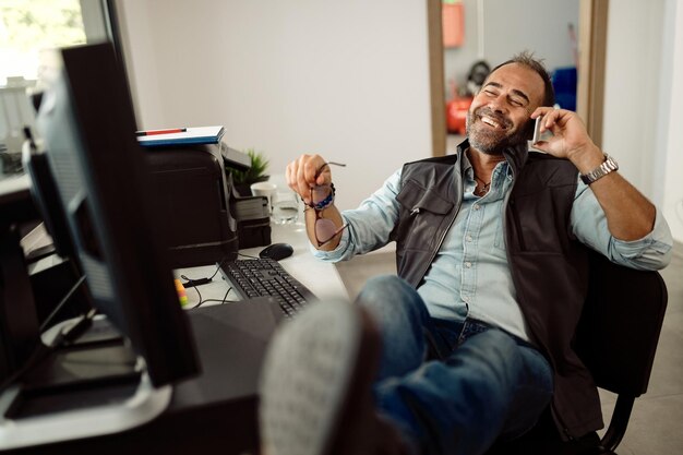 Mecánico feliz haciendo una llamada telefónica mientras se relaja en la oficina de un taller de reparación