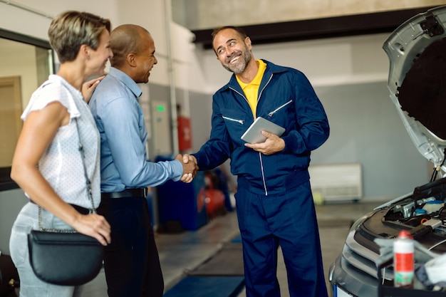 Mecánico feliz saludando a sus clientes en el taller de reparación de automóviles