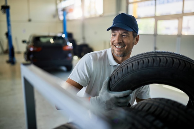 Mecánico feliz trabajando con neumáticos en el taller de servicio de automóviles