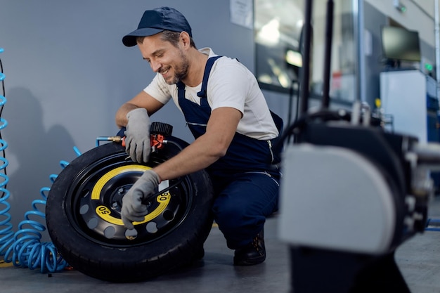 Mecánico feliz usando manómetro mientras repara neumáticos de auto en un taller