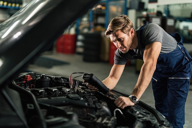 Mecánico joven con herramienta de diagnóstico que analiza el problema del motor del automóvil en el taller de reparación de automóviles