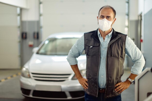 Mecánico con mascarilla protectora de pie en el taller de reparación de automóviles y mirando a la cámara