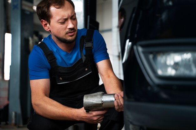 Mecánico masculino que trabaja en un taller de reparación de automóviles en un automóvil