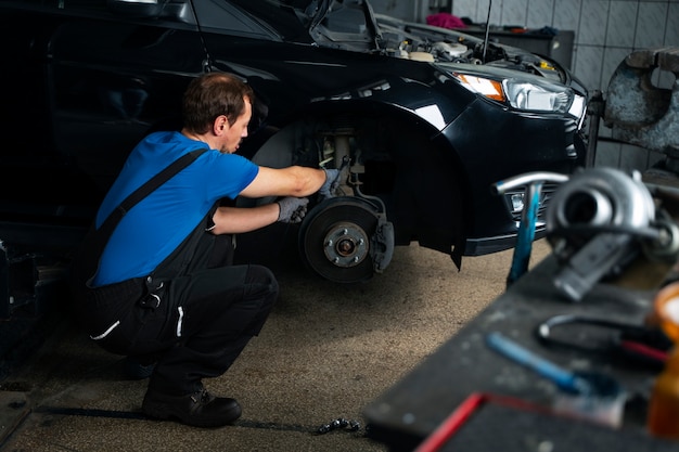 Foto gratuita mecánico masculino que trabaja en un taller de reparación de automóviles en un automóvil