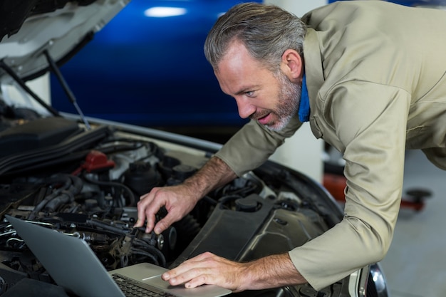 Foto gratuita mecánico que usa la computadora portátil mientras que el servicio de motor de automóvil