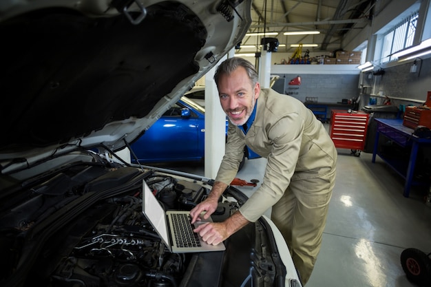 Mecánico que usa la computadora portátil mientras que el servicio de un motor de un coche