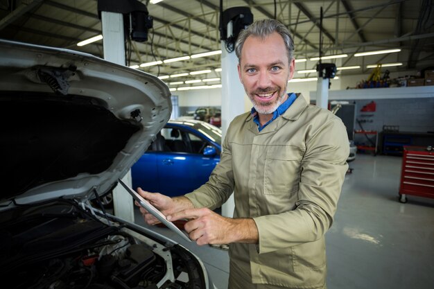 Mecánico que usa la tableta digital durante el servicio de un motor de automóvil