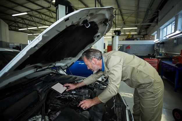 Mecánico que usa la tableta digital durante el servicio de un motor de automóvil