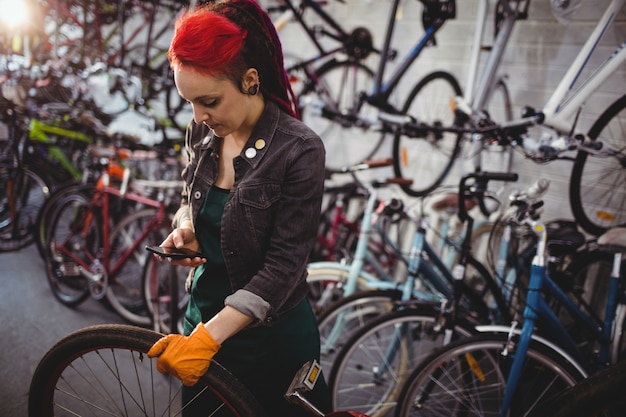 Mecánico que usa el teléfono móvil durante la reparación de la bicicleta