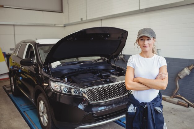 Mecánico de sexo femenino de pie con los brazos cruzados delante del coche